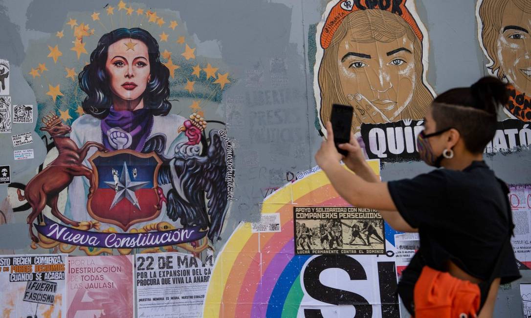 Jovem de máscara tira foto de mural de Santiago em apoio à redação de uma nova Constituição, tema de plebiscito realizado hoje no Chile Foto: MARTIN BERNETTI / AFP