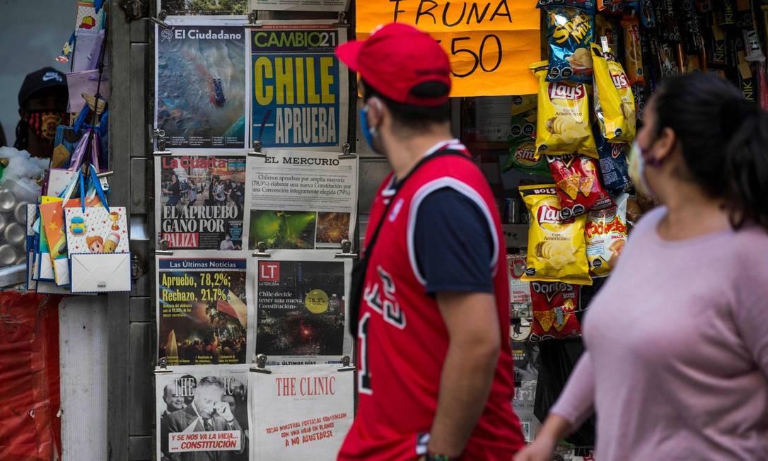 Transeuntes passam em frente a banca de jornal em Santiago onde publicações anunciam o resultado do plebiscito constituinte Foto: JAVIER TORRES / AFP