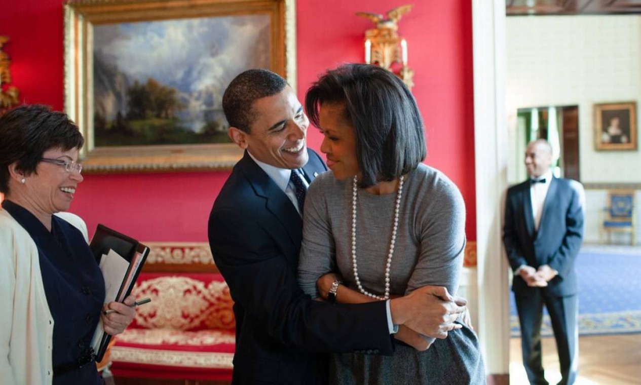 Barack Obama abraça a primeira-dama Michelle Obama na sala vermelha da Casa Branca, com a assessora sênior Valerie Jarret, em foto de 2009 Foto: Pete Souza / Casa Branca 20-3-09