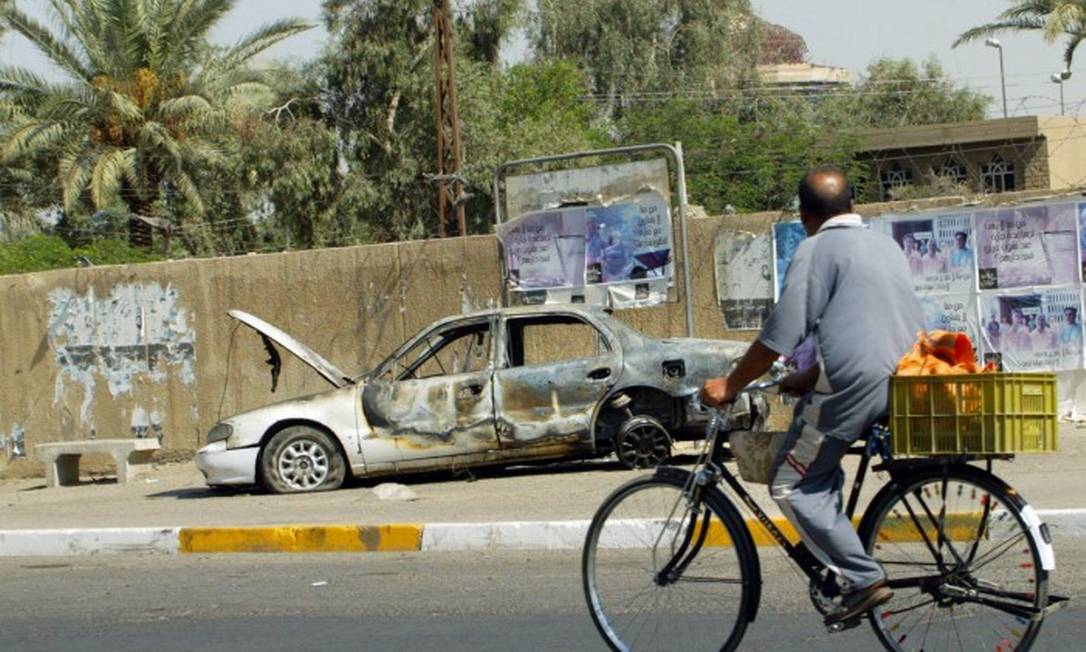 Em 20 de setembro de 2007, um iraquiano anda de bicicleta passando por restos de um carro, queimado depois que guardas da Blackwater abriram fogo e cometeram um massacre contra civis em Bagdá Foto: ALI YOUSSEF / AFP