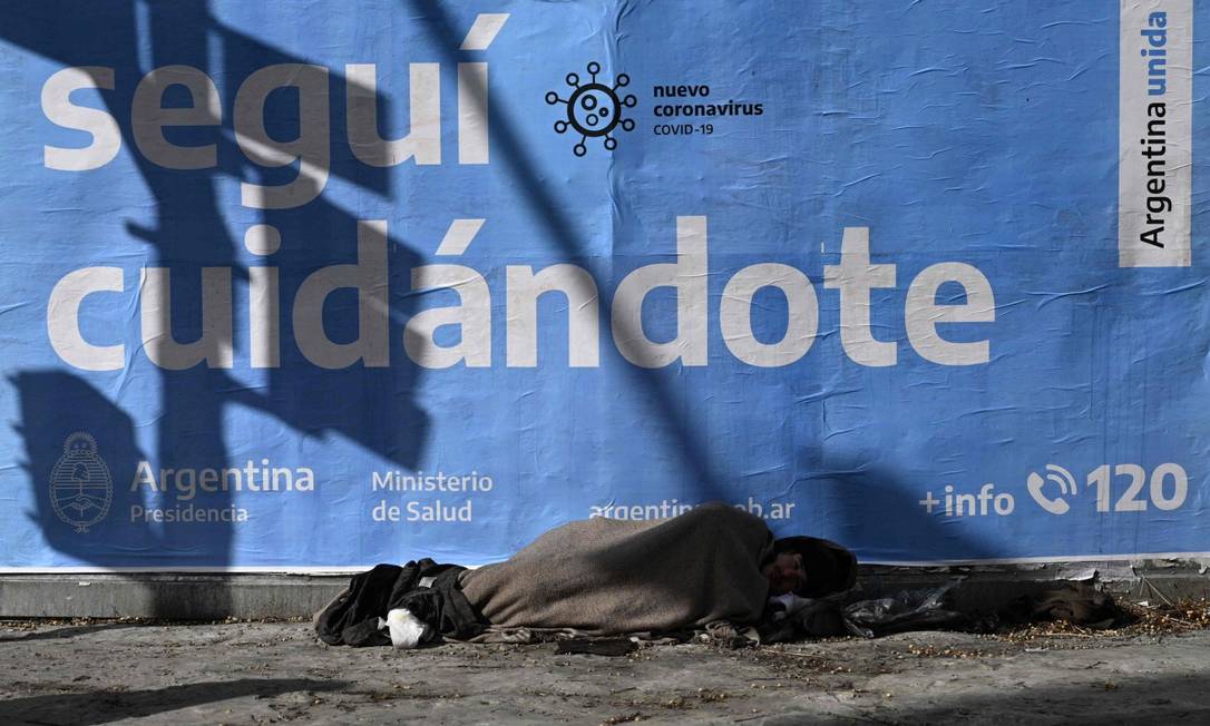 Homem sem teto dorme em frente a cartaz divulgando medidas de proteção na Argentina Foto: JUAN MABROMATA / AFP 24-7-21