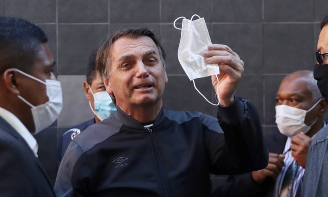 O presidente Jair Bolsonaro segura uma máscara com a mão em vez de utilizá-la em um espaço movimentado: ao minimizarem vírus, líderes incentivam cidadãos a não levar vírus a sério, diz estudo Foto: AMANDA PEROBELLI / Reuters