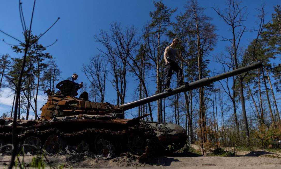 Moradores sobem sobre tanque russo destruído em Irpin, na Ucrânia Foto: CARLOS BARRIA / REUTERS