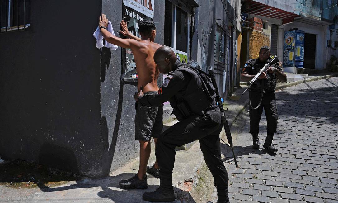Morador do Morro do Banco é revistado por um policial durante a ação na comunidade: pela previsão do estado, favela será uma das primeiras a ter a regulamentação fundiária Foto: Carl de Souza / AFP